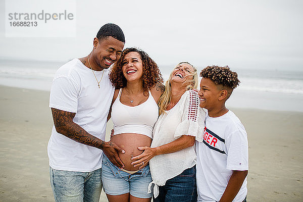 Familie posiert und lacht für Mutterschaftsfotos am Strand