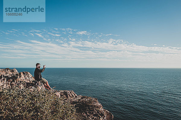 Junger Mann fotografiert das Meer von einer Klippe in Sagres  Portugal