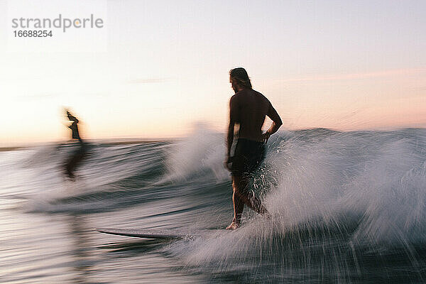 Zwei Freunde surfen auf Longboards bei Sonnenuntergang im Sommer