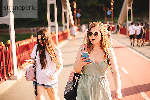Zwei junge Frauen mit Smartphones auf einer Brücke im Sommer