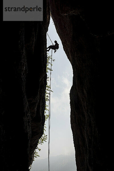 Silhouette einer Bergsteigerin beim Abseilen an einem Riss im Berg