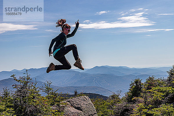Junge sportliche Frau  die auf dem Gipfel eines Berges in Pose springt.