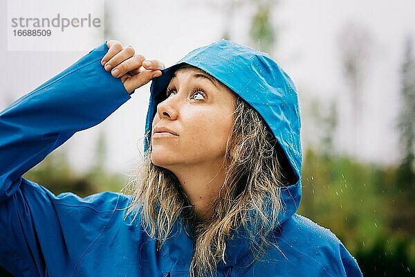 Frau  die im Regen steht und mit einem Regenmantel in den Himmel schaut