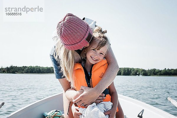 Mutter umarmt glückliche Tochter auf einem Boot im Sommer in Schweden