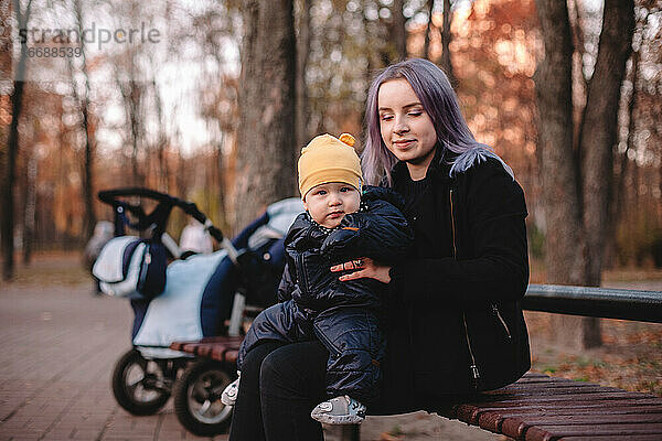 Glückliche junge Mutter mit ihrem kleinen Sohn auf einer Bank im Park sitzend
