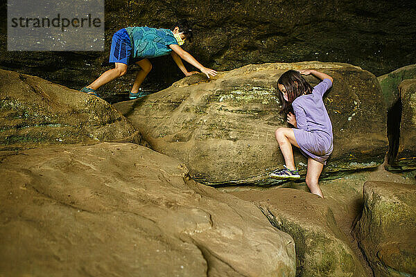 Zwei Kinder mit Gesichtsmasken klettern über große Sandsteinblöcke