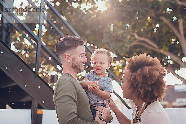 Der Vater hält den kleinen Jungen und die Mutter versucht  ihn zum Lachen zu bringen