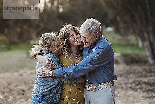 Porträt einer erwachsenen Frau und älterer Eltern  die sich im Park umarmen