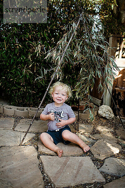 Zwei Jahre alter Junge sitzt unter Bambus und lächelt für die Kamera
