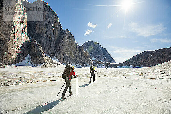 Zwei Rucksacktouristen wandern auf einem Gletscher unterhalb steiler Berge.