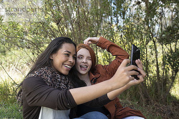 zwei gemischtrassige Frauen machen ein Selfie im Park