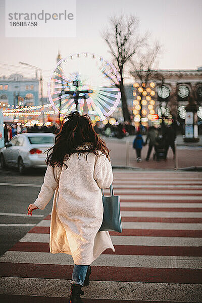 Rückansicht einer jungen Frau beim Überqueren der Straße in der Stadt im Winter