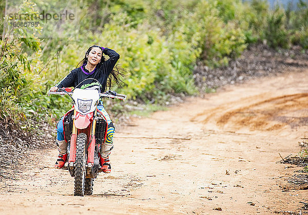 Frau fährt mit ihrem Geländemotorrad auf einem Waldweg in Pak Chong / Thailand