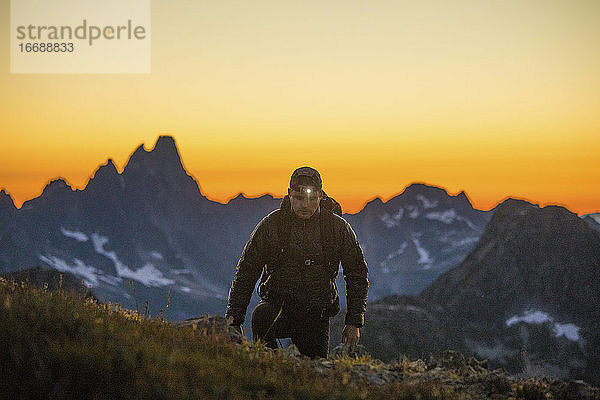 Wanderer steigt nach Sonnenuntergang mit Stirnlampe auf einen Berg.