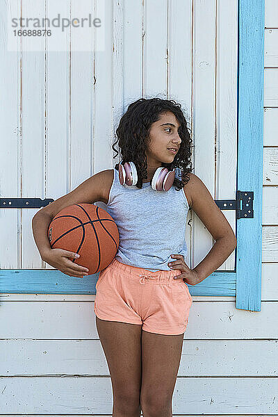 Porträt eines Mädchens mit lockigem Haar mit einem Basketball und Kopfhörern