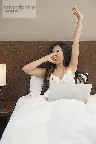 schöne Frau wacht auf und überprüft ihren Laptop im Hotelzimmer