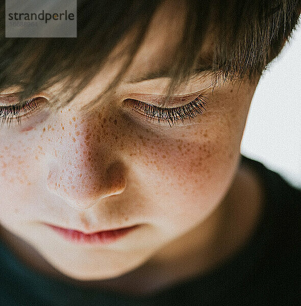 Nahaufnahme des Gesichts eines kleinen Jungen mit Sommersprossen  der nach unten schaut.