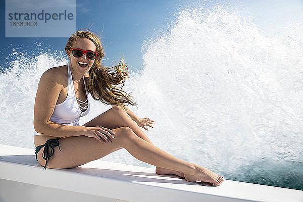 Fröhliche junge Frau  die auf einem Boot sitzt  während im Hintergrund die Wellen plätschern