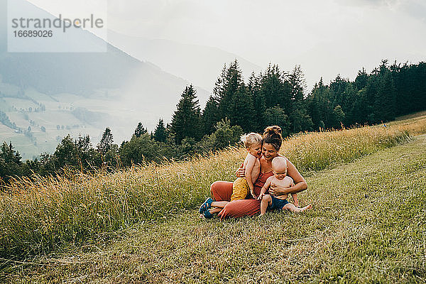 Mutter und Kinder umarmen sich in den Bergen auf dem Boden sitzend