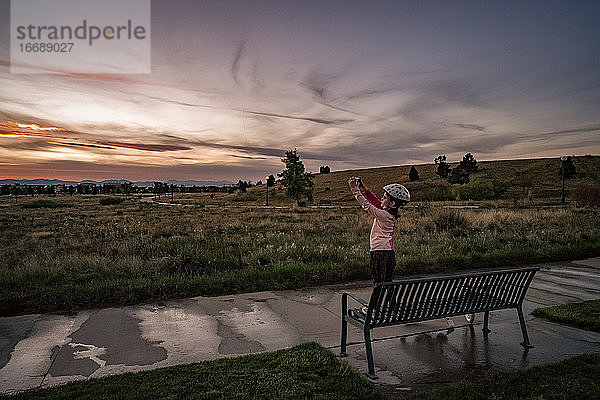 ein konzentriertes junges Mädchen fotografiert den Sonnenuntergang in einem Park