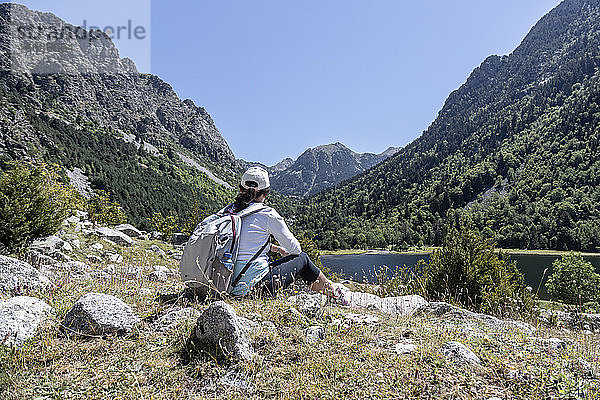 Weibliche Rucksacktouristin in Spanien betrachtet die Landschaft  während sie auf einem Felsen vor einem See sitzt.