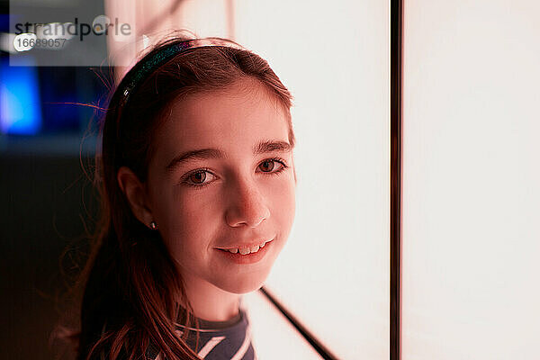 Porträt eines lächelnden Mädchens  das in eine Kamera neben einer beleuchteten Wand blickt