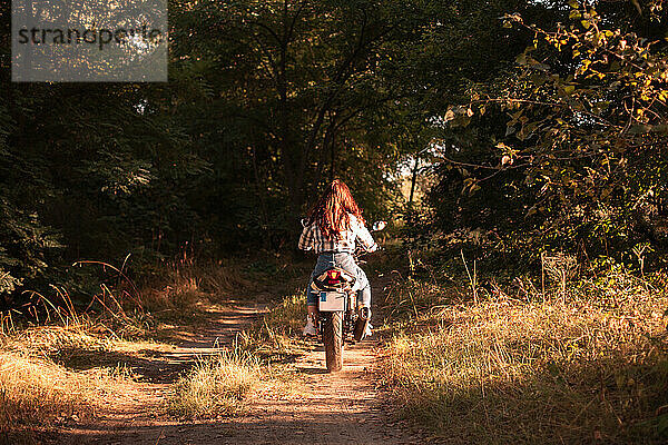 Rückansicht einer Frau  die auf einem unbefestigten Weg im Wald Motorrad fährt