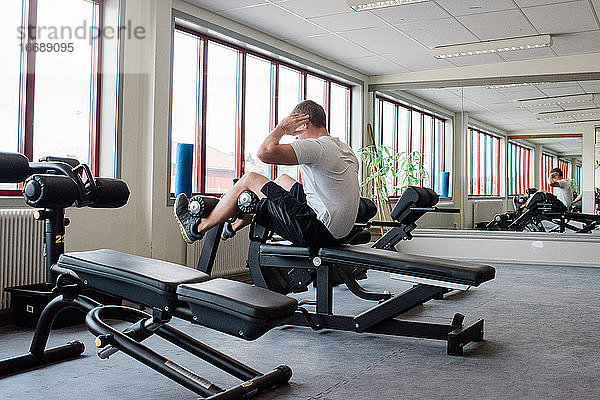 Mann macht Sit-ups an einem Gerät und trainiert seine Bauchmuskeln im Fitnessstudio