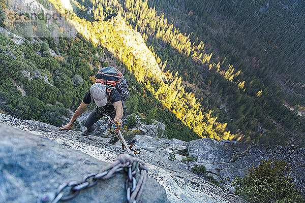 Mann mit Hut  der nach unten schaut  jongliert Seil mit Rucksack am El Capitan hoch