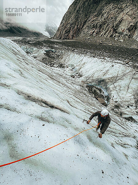 Hochformatige Aufnahme eines Mannes  der mit Eispickeln eine steile Eiswand erklimmt