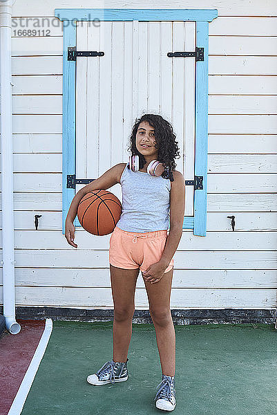 Ein kleines Mädchen mit lockigem Haar und einem Basketball schaut in die Kamera