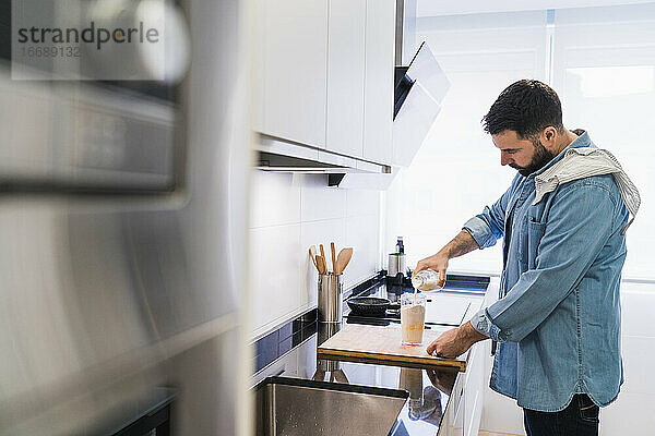 Mann im Jeanshemd beim Kochen in der Küche. Ein Mann gießt Milch in einen Behälter