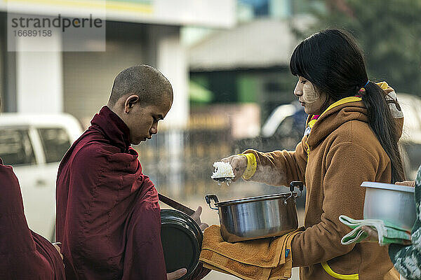Eine burmesische Frau gibt einem Mönch einen Löffel mit gedämpftem Reis  Nyaung U  Myanmar