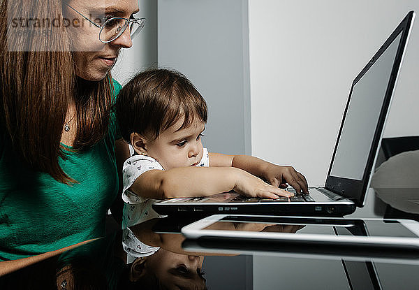 Beschäftigte Frau mit kleinem Kind arbeitet am Laptop