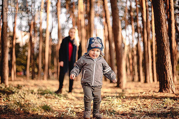 Ein kleiner Junge geht im Herbst im Park spazieren  seine Mutter steht hinter ihm