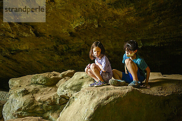 zwei kleine ernste Kinder sitzen zusammen auf einem Felsvorsprung in einer Schlucht