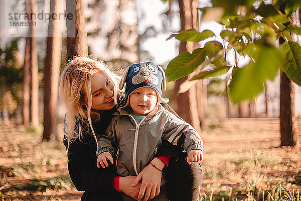 Glückliche junge Mutter umarmt ihr kleines Kleinkind Sohn im Park im Herbst