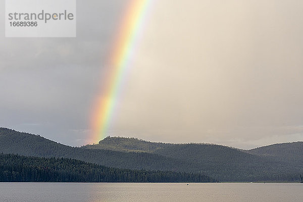 Ein leuchtender Regenbogen über einem ruhigen See und bewaldeten Bergen
