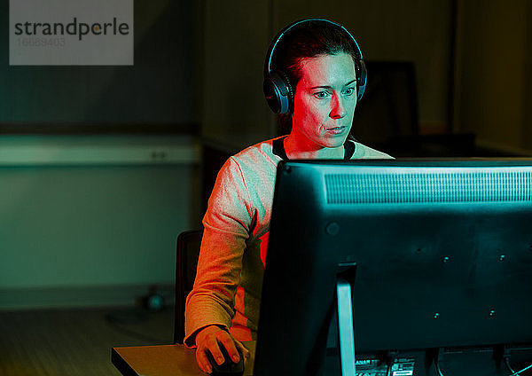 Eine Frau mit Computermaus in der Hand arbeitet am Computer in einem dunklen Raum