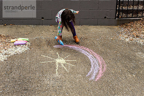 Kleines Mädchen malt Regenbogen mit Kreide