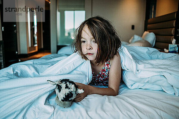 junges Mädchen im Hotelbett  das mit seinem Spielzeug aus dem Mittagsschlaf erwacht
