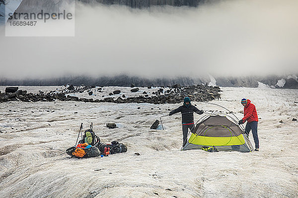 Zwei Männer schlagen ein Zelt unterhalb eines dramatischen Berggipfels auf.