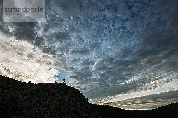 Person auf Berg in Silhouette mit dramatischen Wolken in Maine