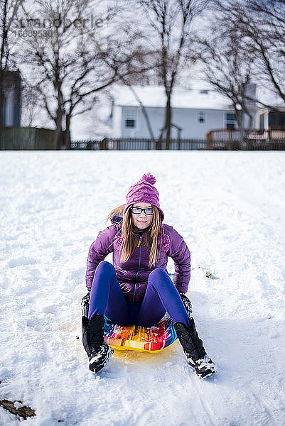 Pre-Teenie auf Schlitten im Schnee sitzend im Winter