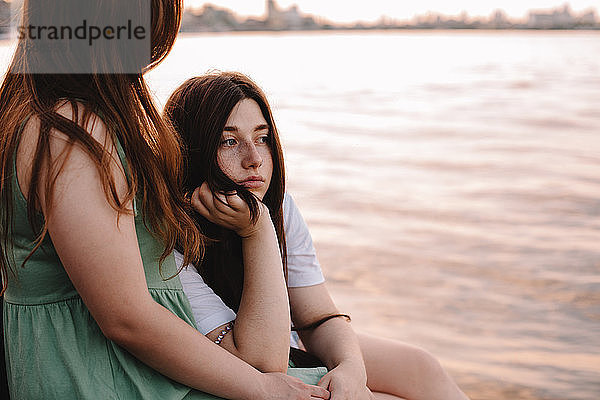 Nachdenkliches lesbisches Paar sitzt am Fluss in der Stadt bei Sonnenuntergang