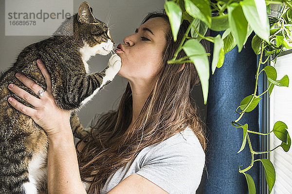 Frau zu Hause  die ihre Katze am Fenster küsst