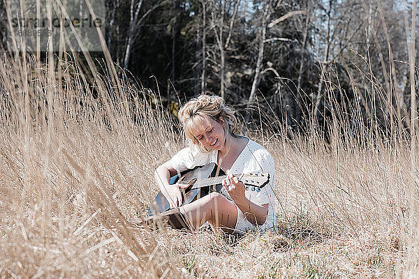 Frau saß auf einem Feld und spielte fröhlich Gitarre im Sommer