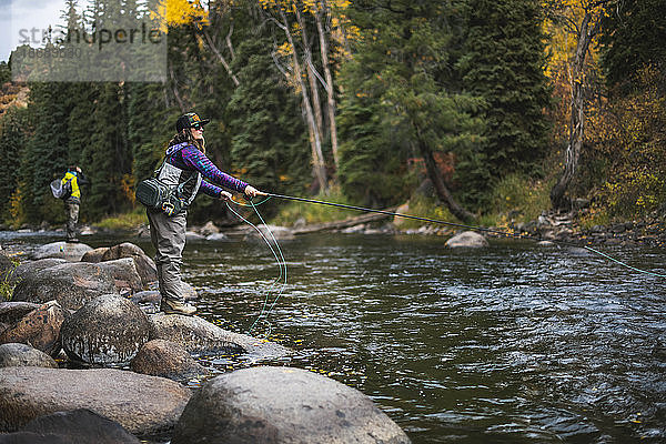 Seitenansicht einer Frau beim Fliegenfischen  die auf einem Felsen am Roaring Fork River steht