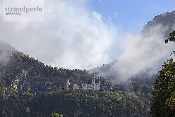 Schloss Neuschwanstein im Nebel an einem Berghang in Deutschland