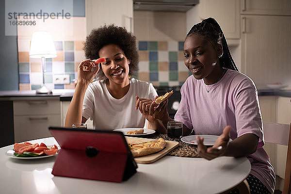 Frauen  die online chatten  während sie sich zu Hause eine Pizza teilen